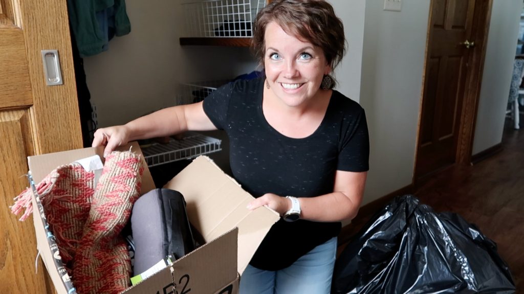 The minimal mom holding donation box next to a trash bag while decluttering